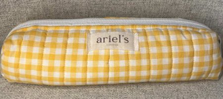 Astuccio in tessuto trapuntato con motivo a quadretti bianchi e gialli, chiuso da una zip bianca, con etichetta centrale 'Ariel's Handmade'.