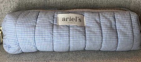 Astuccio a piccoli quadretti azzurri e bianchi in tessuto trapuntato con zip superiore dorata e un'etichetta beige cucita con il marchio 'Ariel's Handmade'.